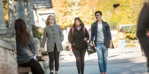 Three students walking together holding bags and laptops on their way to class